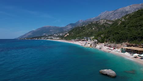 People-Swimming-in-Azure-Sea-and-Sunbathing-on-Dhermi-Beach,-Albania's-Beautiful-Resort-Destination
