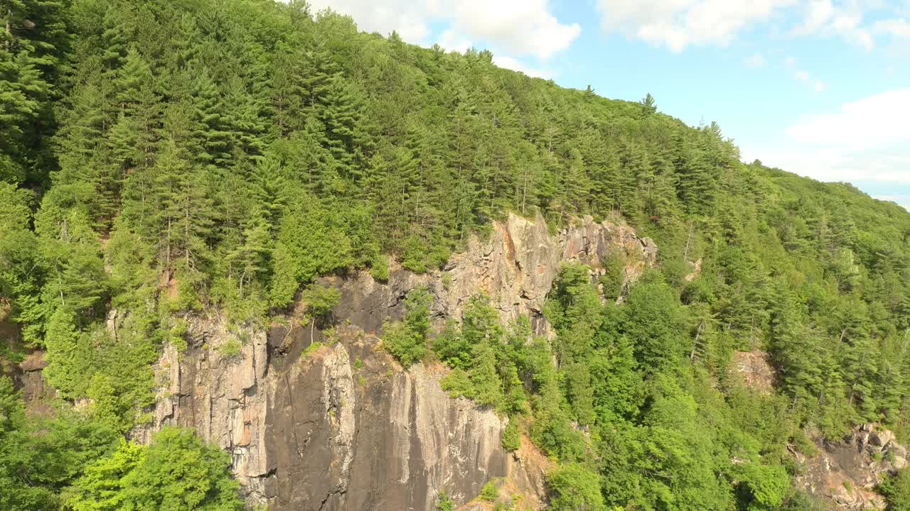 구름이 거의 없는 푸른 하늘에 캐나다의 소나무 숲으로 덮인 수직 절벽