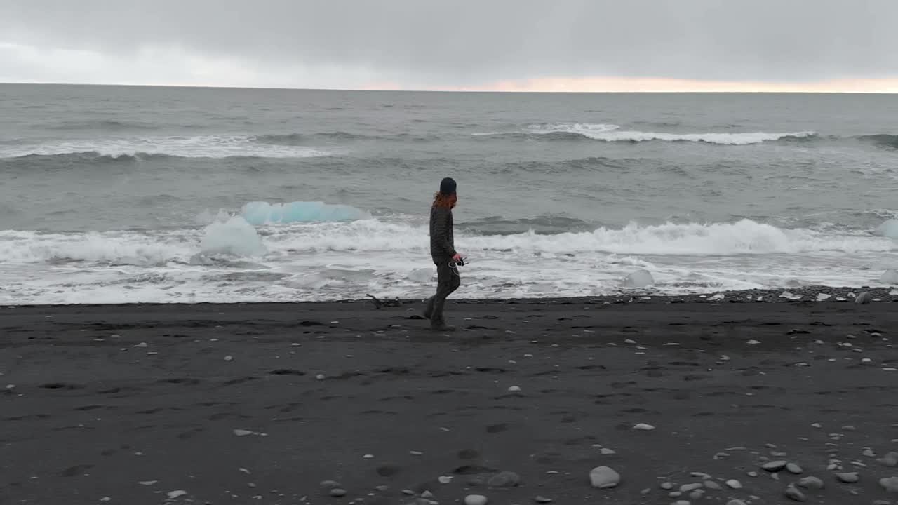 검은 모래 해변을 따라 달리는 공중 프로필 샷