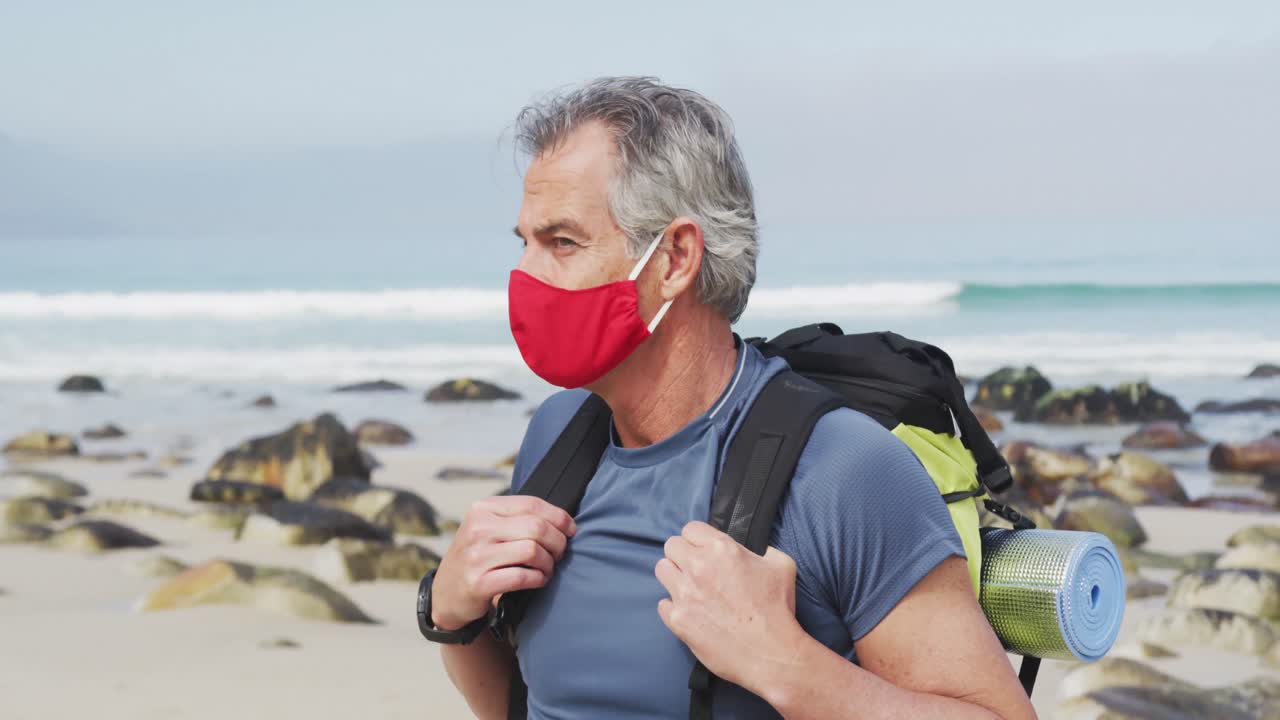 Portrait of senior hiker man wearing face mask with backpack hiking on the beach.
