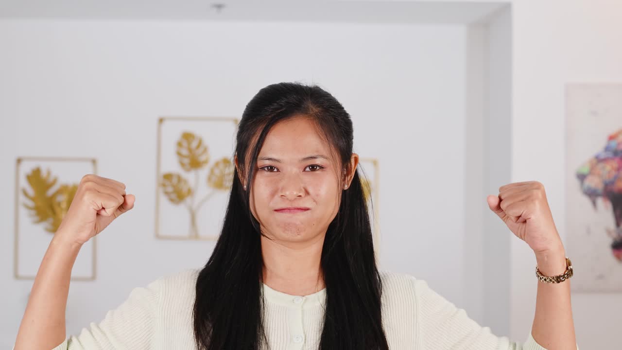 A woman in a bright room flexes her arms, expressing joy and confidence. The atmosphere is uplifting and empowering