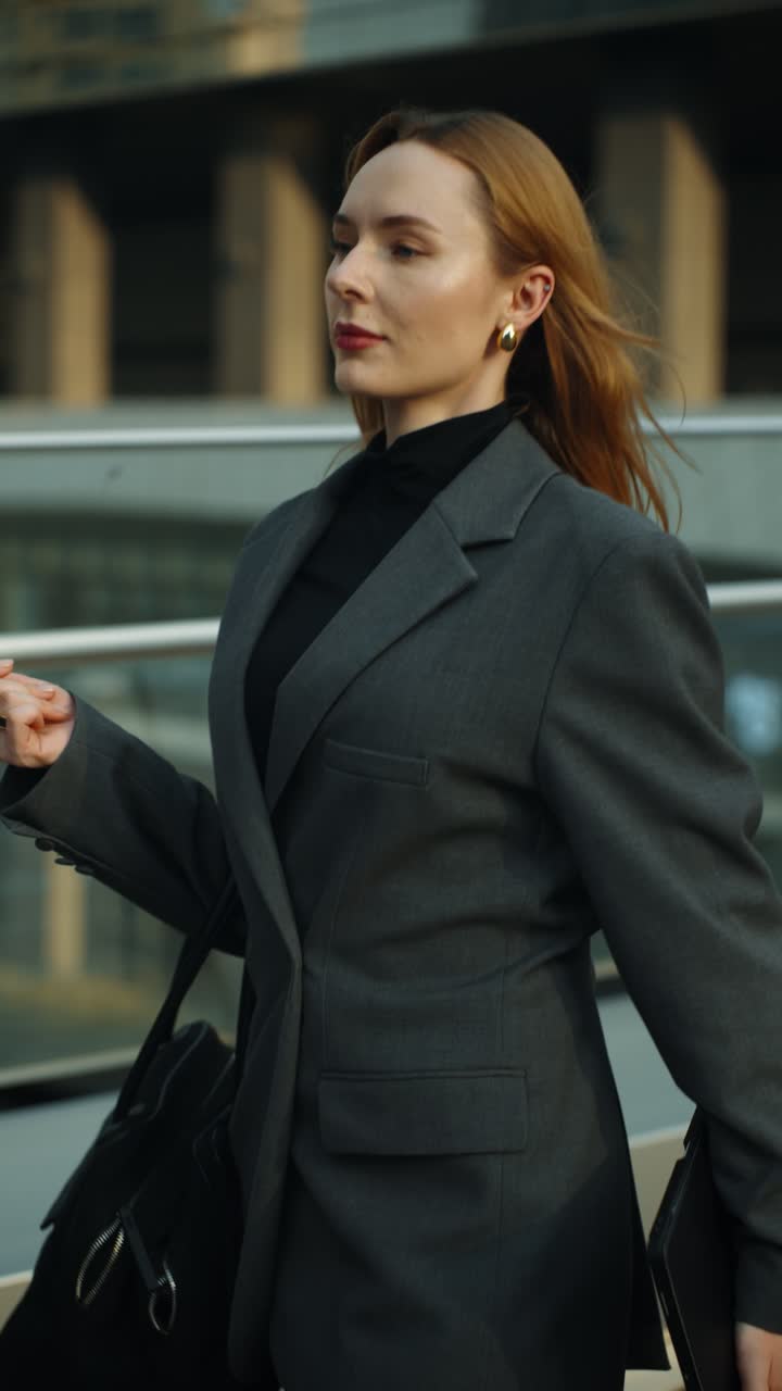 A businesswoman walks along a modern office terrace at sunset, holding a tablet and looking toward the horizon