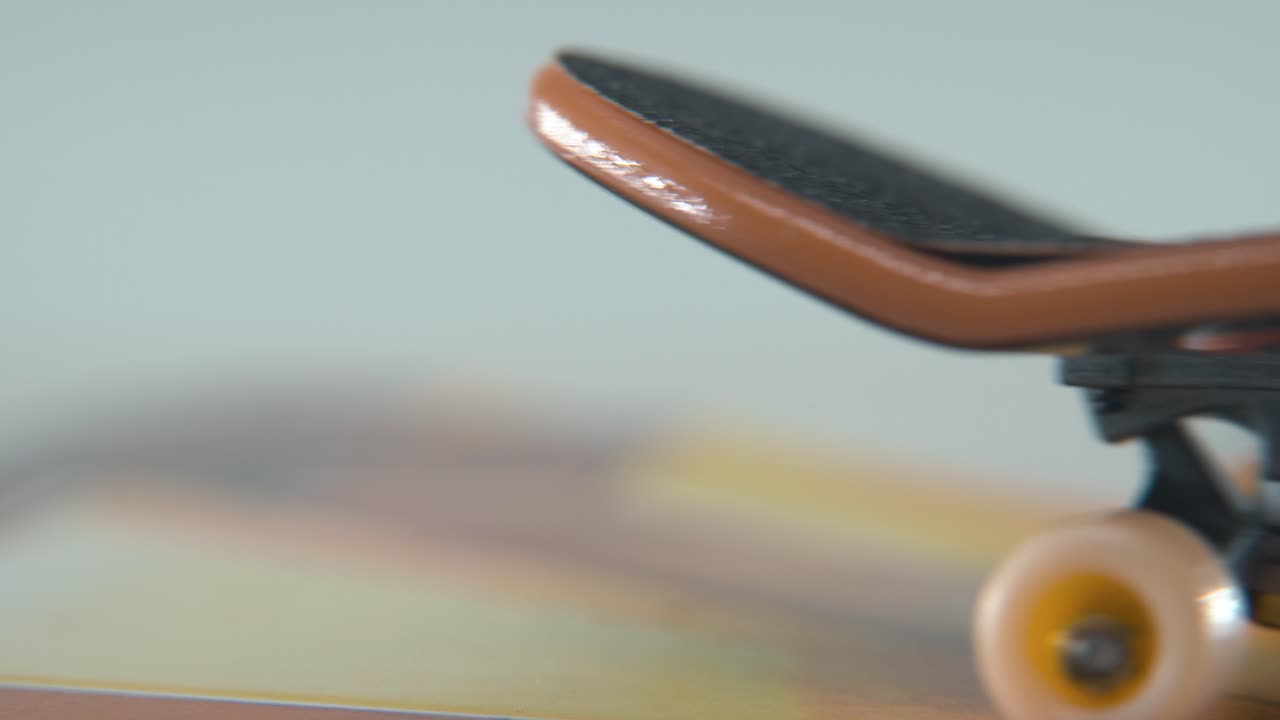 A hyper close-up macro detailed shot of a mini skateboard, tiny white wheels, riding fingerboard from right to left, finger slide, professional lighting, beautiful cinematic 4K video