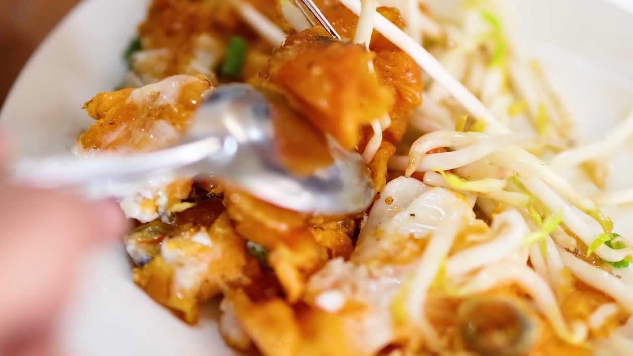 Close-up of hands using utensils to enjoy a crispy pancake topped with fresh bean sprouts.