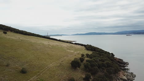 Drohnenschwenk-über-Hügel-Mit-Bohrinsel-Und-Frachtschiff-Im-Hintergrund-Australien