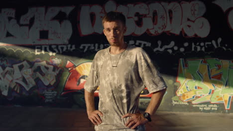 Handsome-man-relaxing-after-training-at-skate-park-with-graffiti-wall.