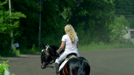 a beautiful girl in white hair and white clothes slowly rides on a black brown stallion. the girl finished training and goes to the recreation area. the girl is a little tired and sweat is visible on her face. sunny summer day on a green glade.