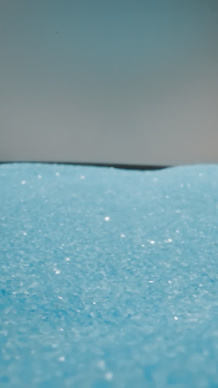 Shiny light blue sand shuddering from jolts on grey background. Tiny particles of sand glittering and shimmering at bright studio light macro