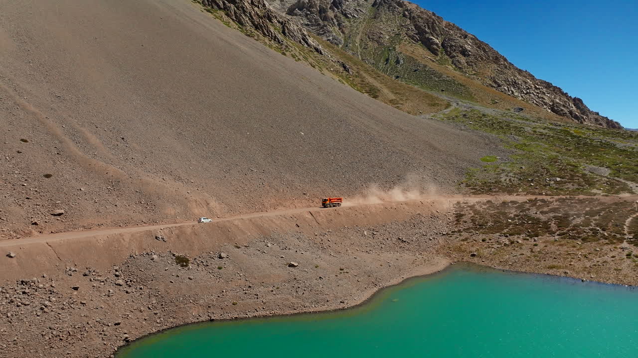 Truck kicks up dust on dirt road next to Embalse Del Yeso lake, aerial