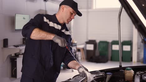 Car-mechanic-checking-oil-level-of-car-engine-in-workshop