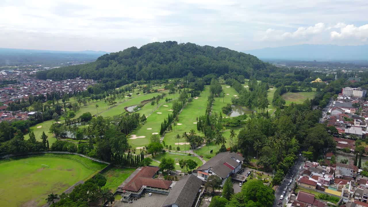 Vista aérea de un campo de golf verde en un día soleado con un pequeño estanque en medio de la ciudad.
