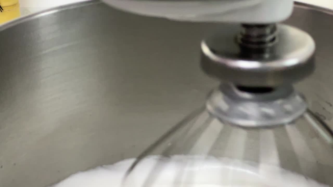 Electric mixer mixing egg white and sugar until it is glossy peak and stiff peak, preparing meringue buttercream in commercial setting close up shot