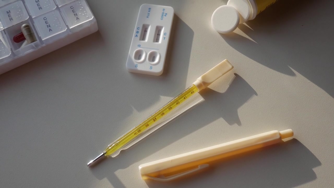 Zoom indietro da un tavolo medico con termometro, test COVID, penna e pillole