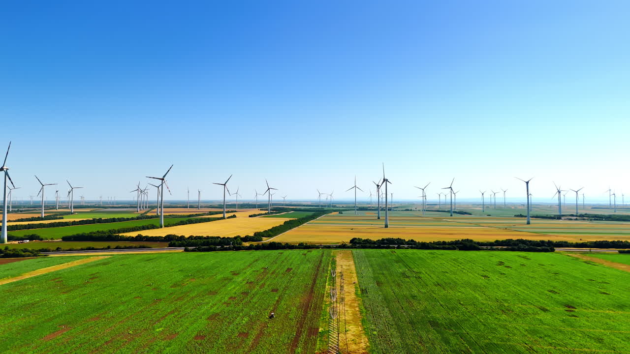 Turbines rise in green fields. Wind turbines rotate above lush green fields under a clear blue sky, illustrating sustainable energy in a rural area