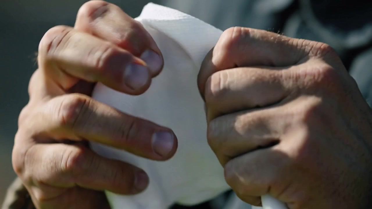 Pressing adult hands pulling folded white tissue apart outdoors, revealing layers, dark jacket