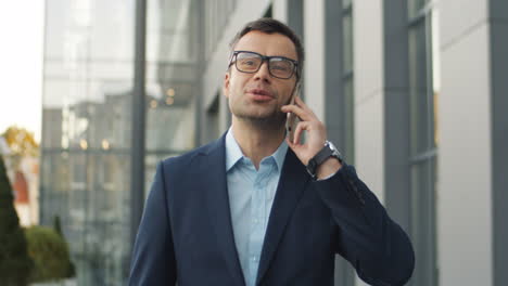 Front-View-Of-Grey-Haired-Businessman-Talking-On-Phone-While-Walking-The-Street