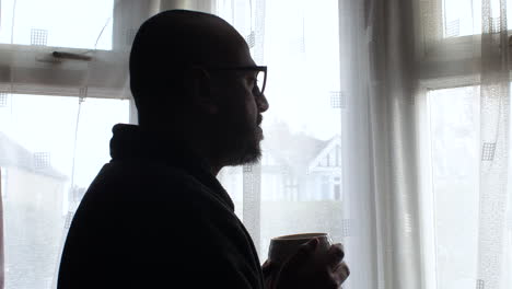 silhouetted man sipping coffee by the window, reflecting in a moment of solitude, morning light