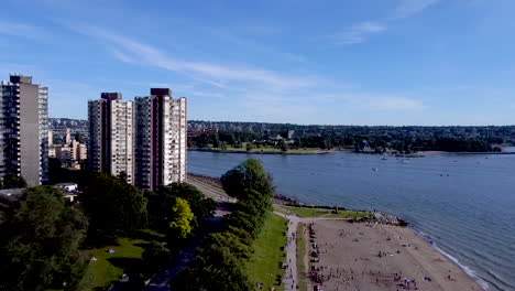 Aerial floyover semi crowded tropical beach by residential towers parks people are respectfully distancing each other by 6 feet while suntannin lounging cuddling biking dancing eating swimming walking
