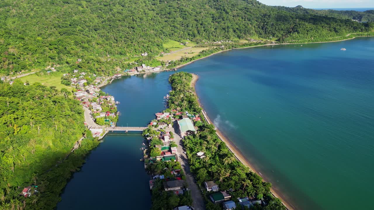 Stunning overhead drone shot of lush, hillside barangay village facing estuary and pristine cove waters during daytime - Batalay, Bato, Philippines