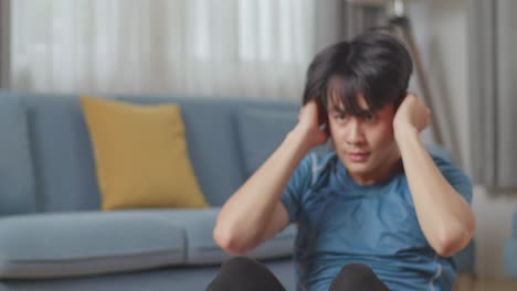 스포츠 옷을 입은 체력 있는 아시아인 남자가 넓고 밝은 거실에서 복부 운동을 하고 있다.