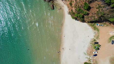 top down aerial view over paradise beach with crystal clear water and waves slowly hitting the shoreline, massive cliffs surrounded by lush green vegetation, thassos, greece, europe