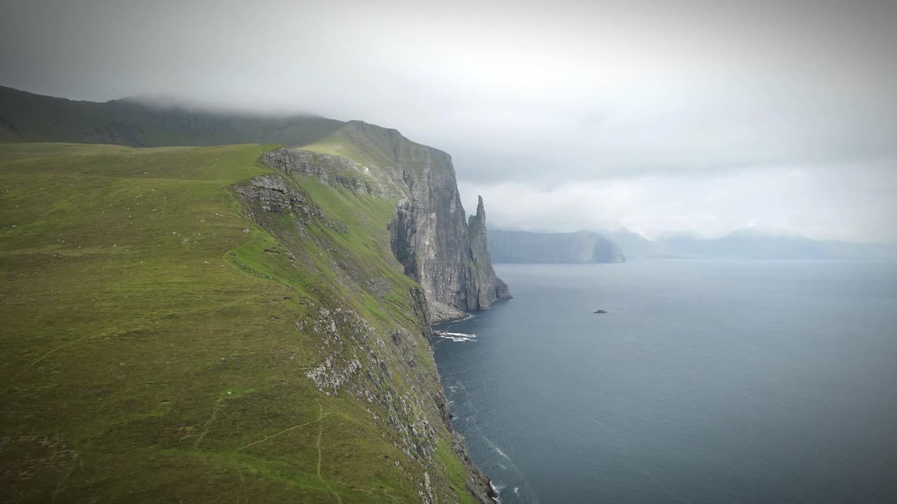 majestuosos acantilados se encuentran con el océano atlántico en trøllkonufingur, islas feroe. colinas verdes onduladas contrastan con formaciones rocosas escarpadas, ofreciendo un paisaje costero sereno y dramático