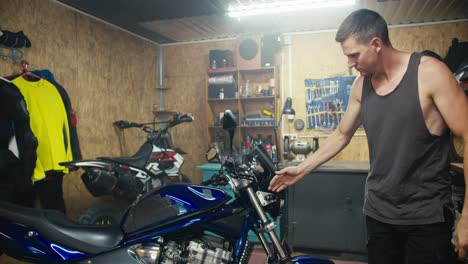 un mecánico masculino con una camisa gris inspecciona una motocicleta azul en su taller de garaje. trabajando con equipos en un garaje de madera equipado con herramientas