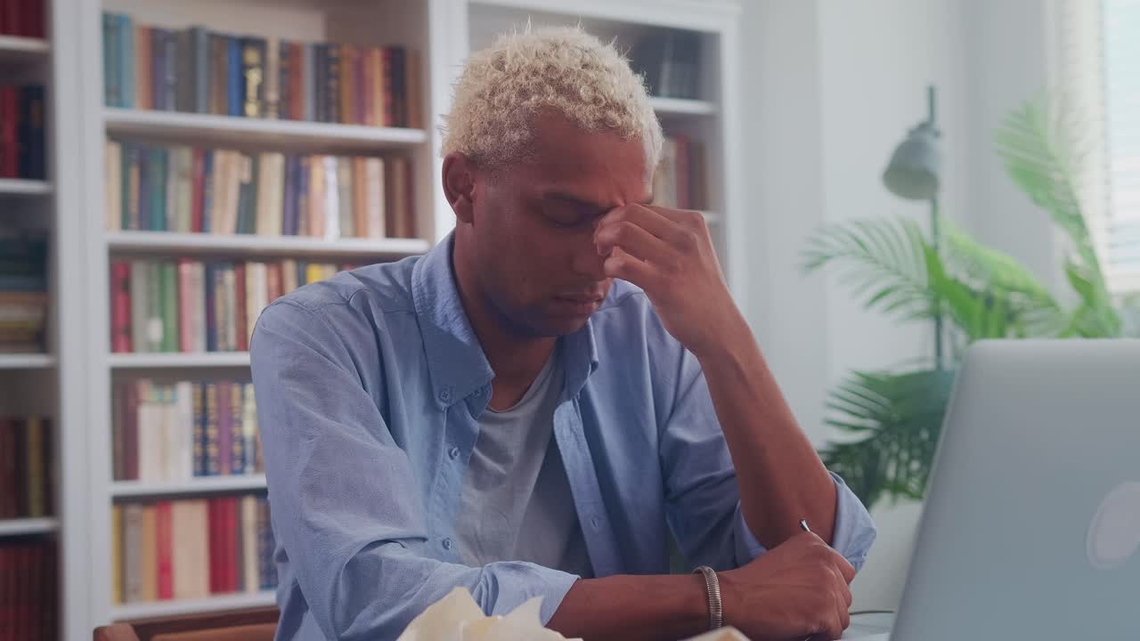 Young african american man sits in office with eyes closed is stressed
