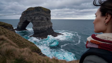 woman admiring a dramatic sea arch on the rugged irish coast