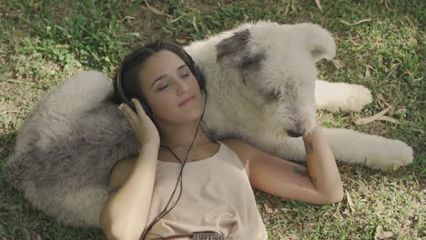 young woman with headphones pets a big dog lying on the grass