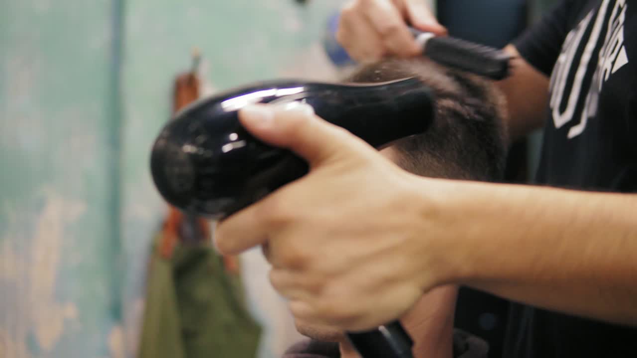 Close Up view of a man sitting in the chair and getting his hair dried in barber shot. Barber styling hair with dryer and