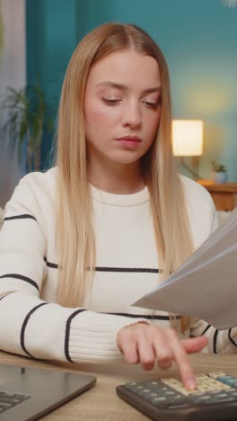 caucasian woman managing tax declaration at home on sofa table holding documents calculator laptop