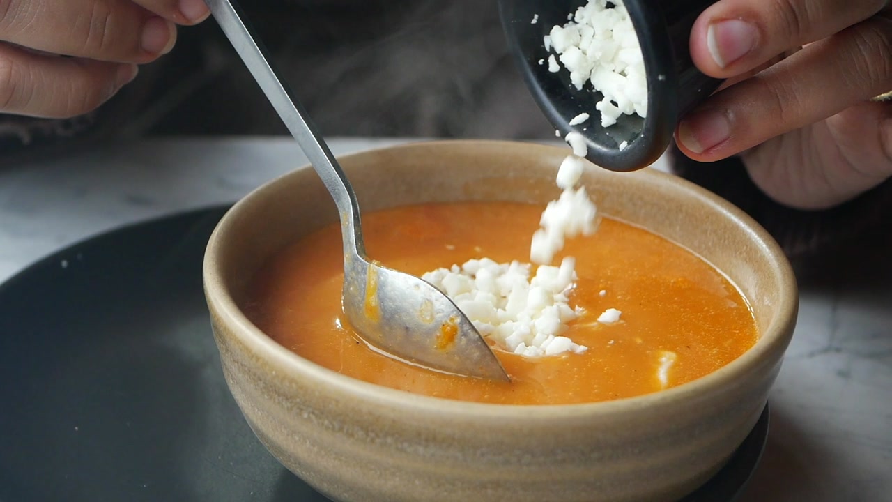 Close-up of Hands Adding Cheese to Steaming Hot Soup