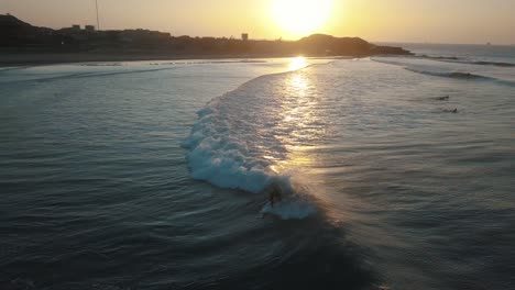 surfer catching a small but long wave during beautiful sunset in peru