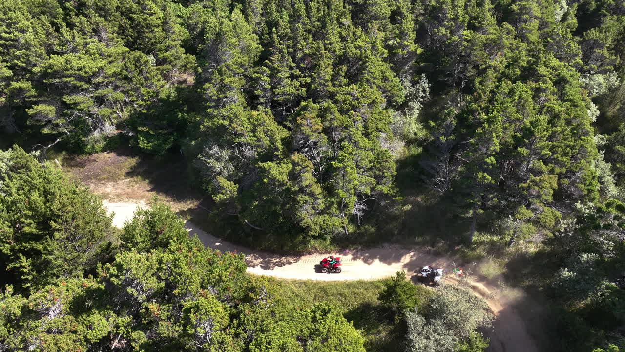 Drone tracking ATV quads on a sand road in middle of a forest, sunny day