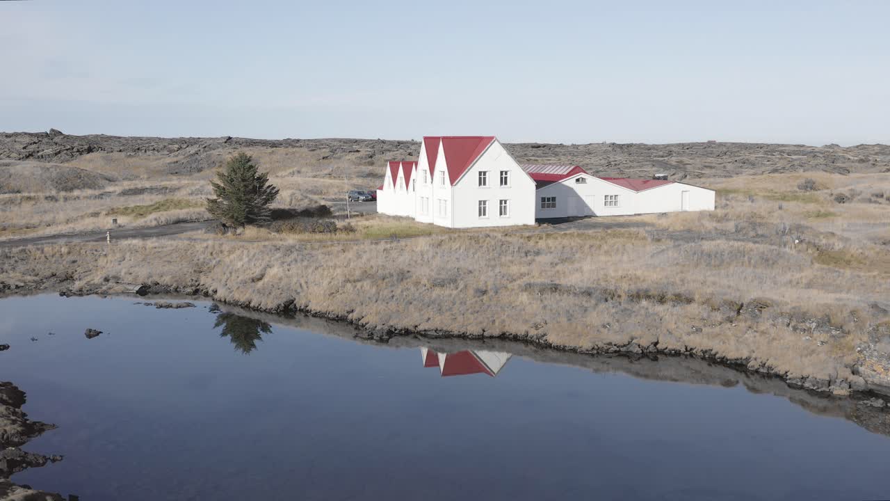 Luftaufnahme eines idyllischen rot-weißen traditionellen Hauses an einem ruhigen See in Island