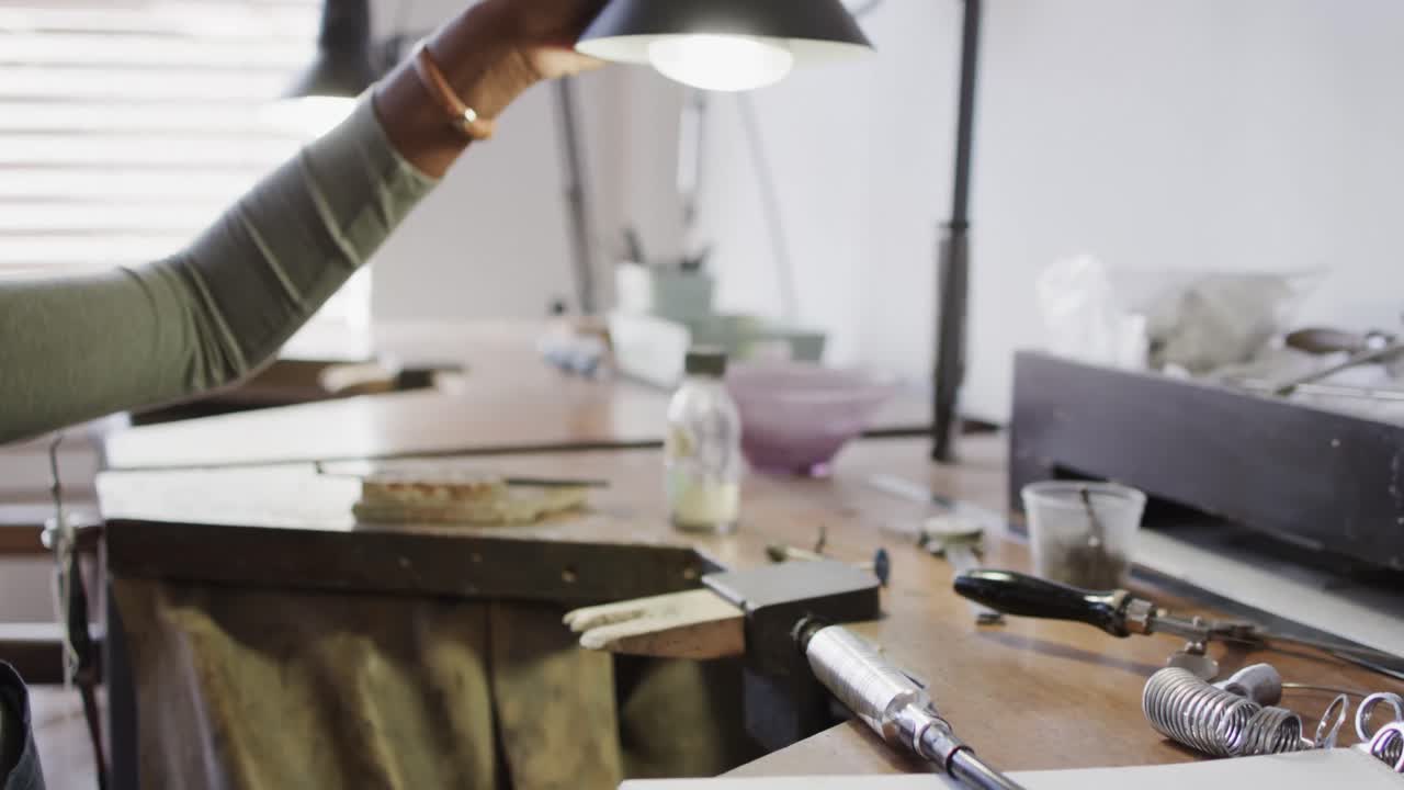 Biracial female worker using handcraft tools in workshop in jewellery studio in slow motion
