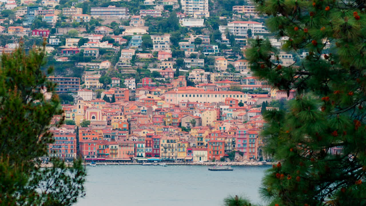 Close up of green tree branches with a blurred, distant view of the colourful buildings of Villefranche-sur-Mer, France