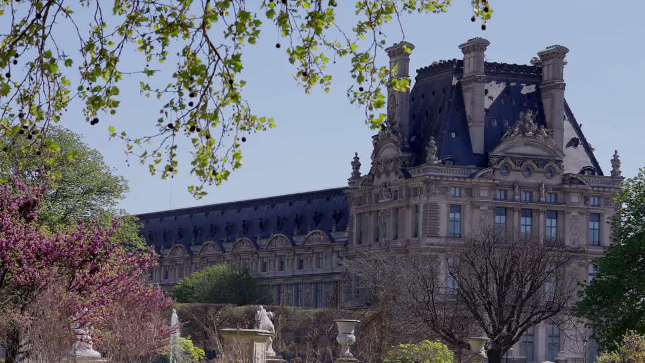 Wide angle view of Louvre Museum facade framed by flowers during summer in Paris.
