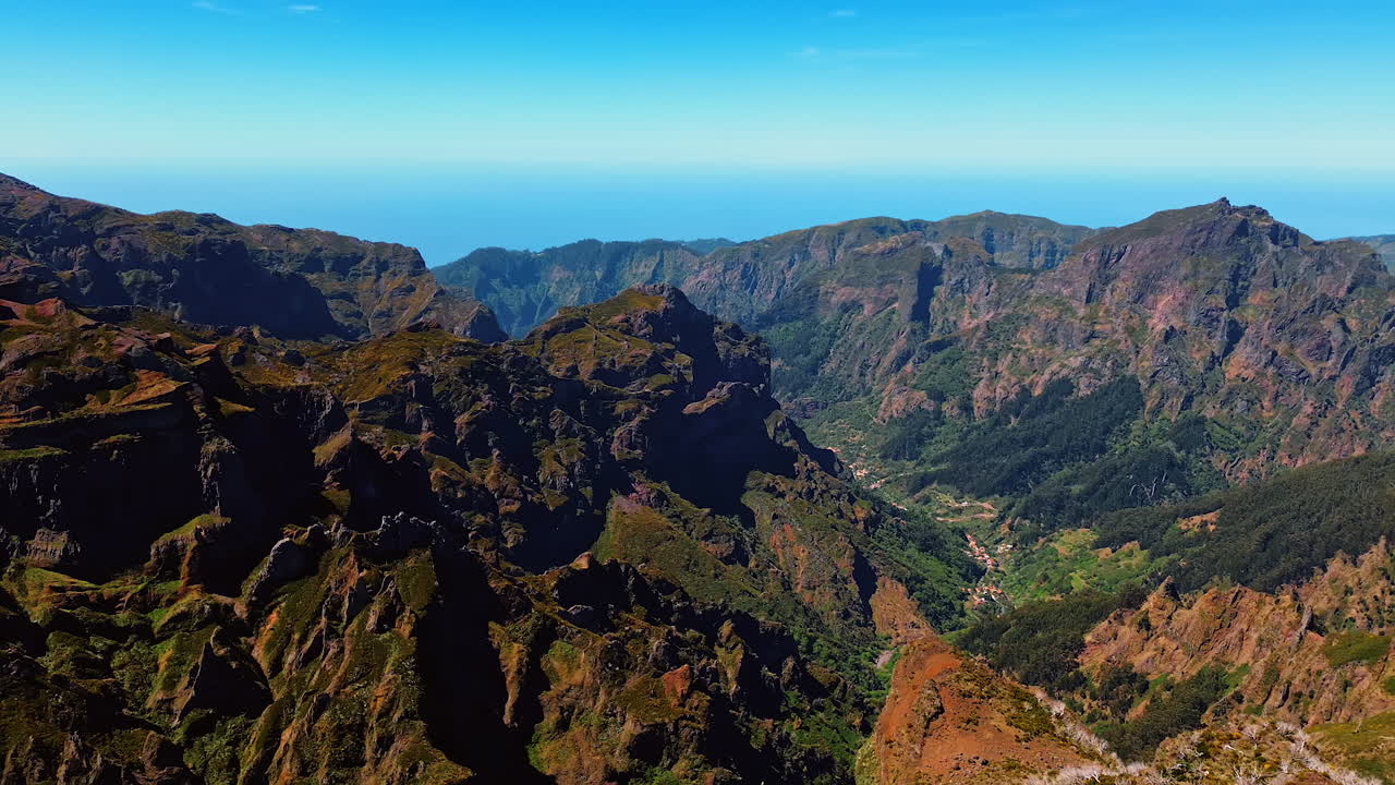 Flight above the barren mountains with greenery growing at the foot. Splendid clear blue sky at backdrop. Madeira Islands, Portugal.