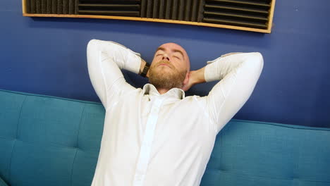 medium shot of a man leaning back and yawning at home on a sofa couch