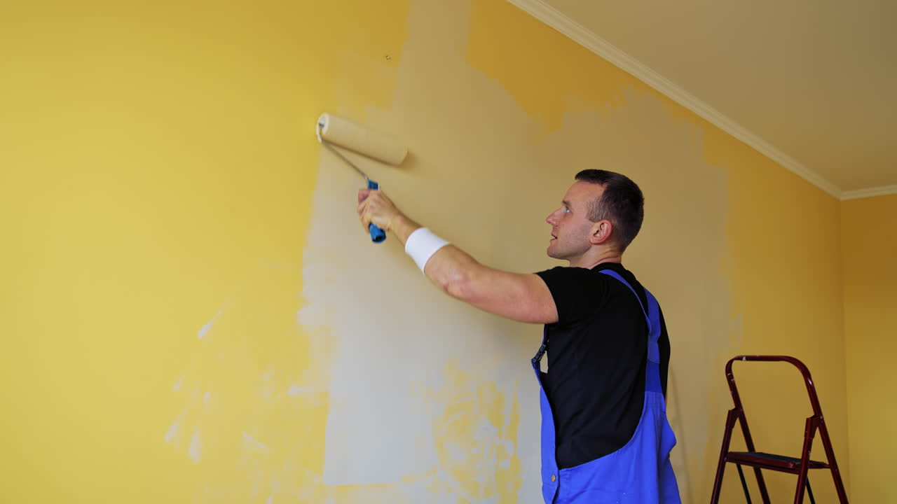 Man with roller painting wall. Young professional male painting wall in new home