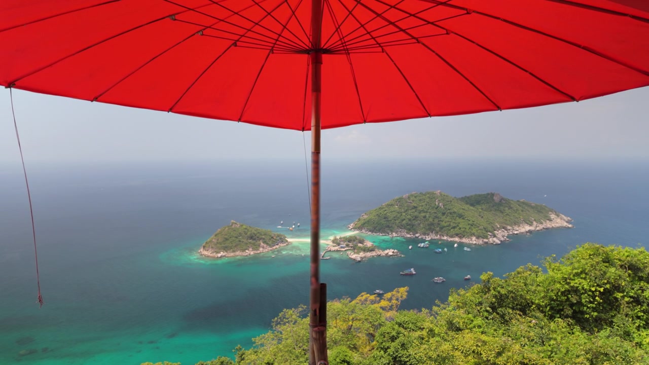 Grande ombrellone rosso offre ombra su una lussureggiante vista sull'isola tropicale e sul mare turchese.