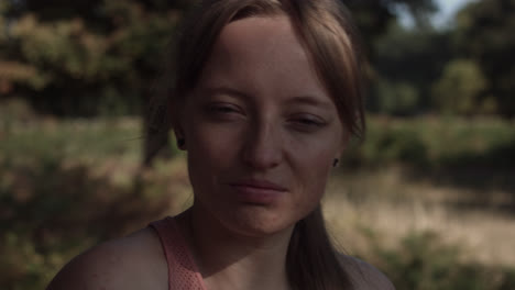 close up of a woman in a park who is standing in the shadow of a tree with the sun shining on her face