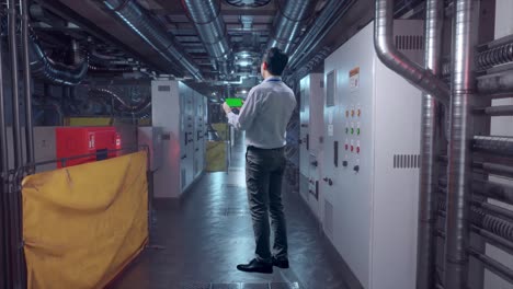 full body back view of an asian male professional worker standing with green screen smartphone in engine control room, industrial facility