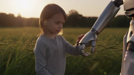 child interacting with a robot's hand in a field at sunset