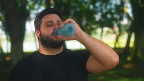 hombre barbudo bebiendo agua después del entrenamiento y corriendo en el parque siendo saludable e hidratado