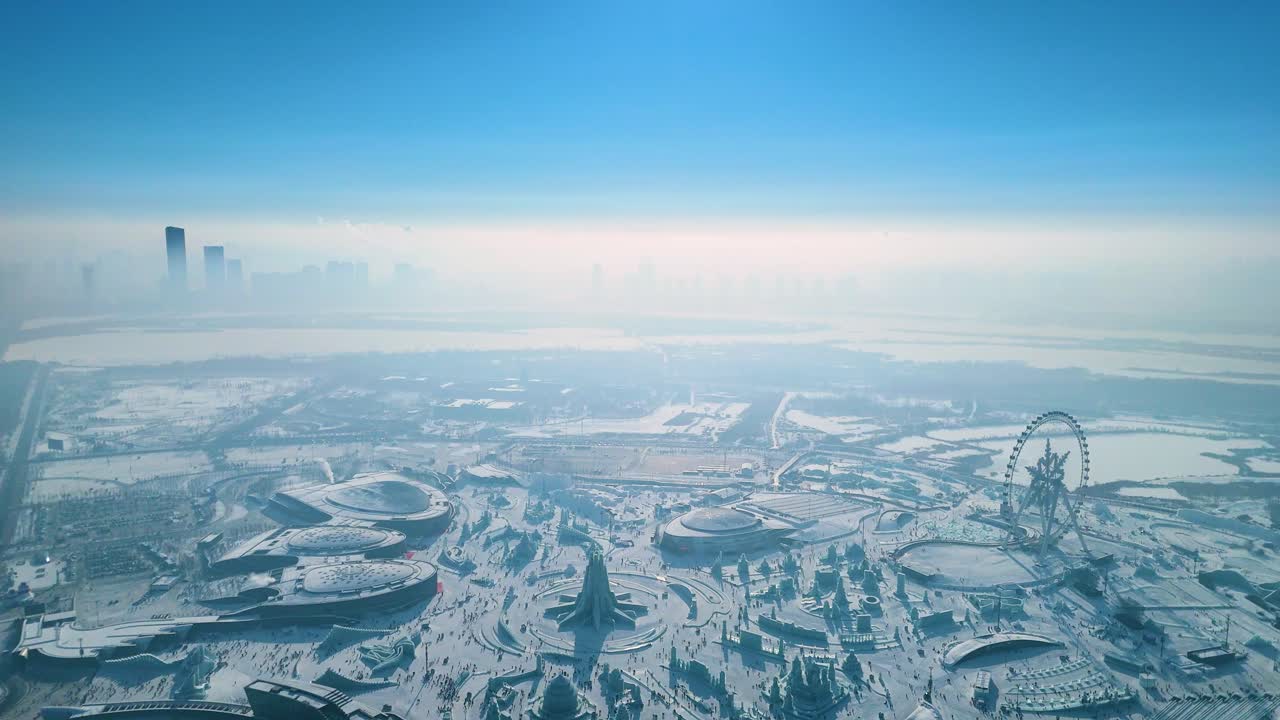 Aerial view of the Harbin Ice Festival 2025, showcasing intricate ice sculptures, frozen palaces, and a vast winter wonderland set against the city skyline under clear blue skies. China