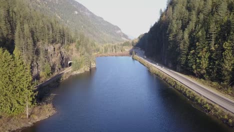 low flight over narrow mountain lake with highway and train tunnel