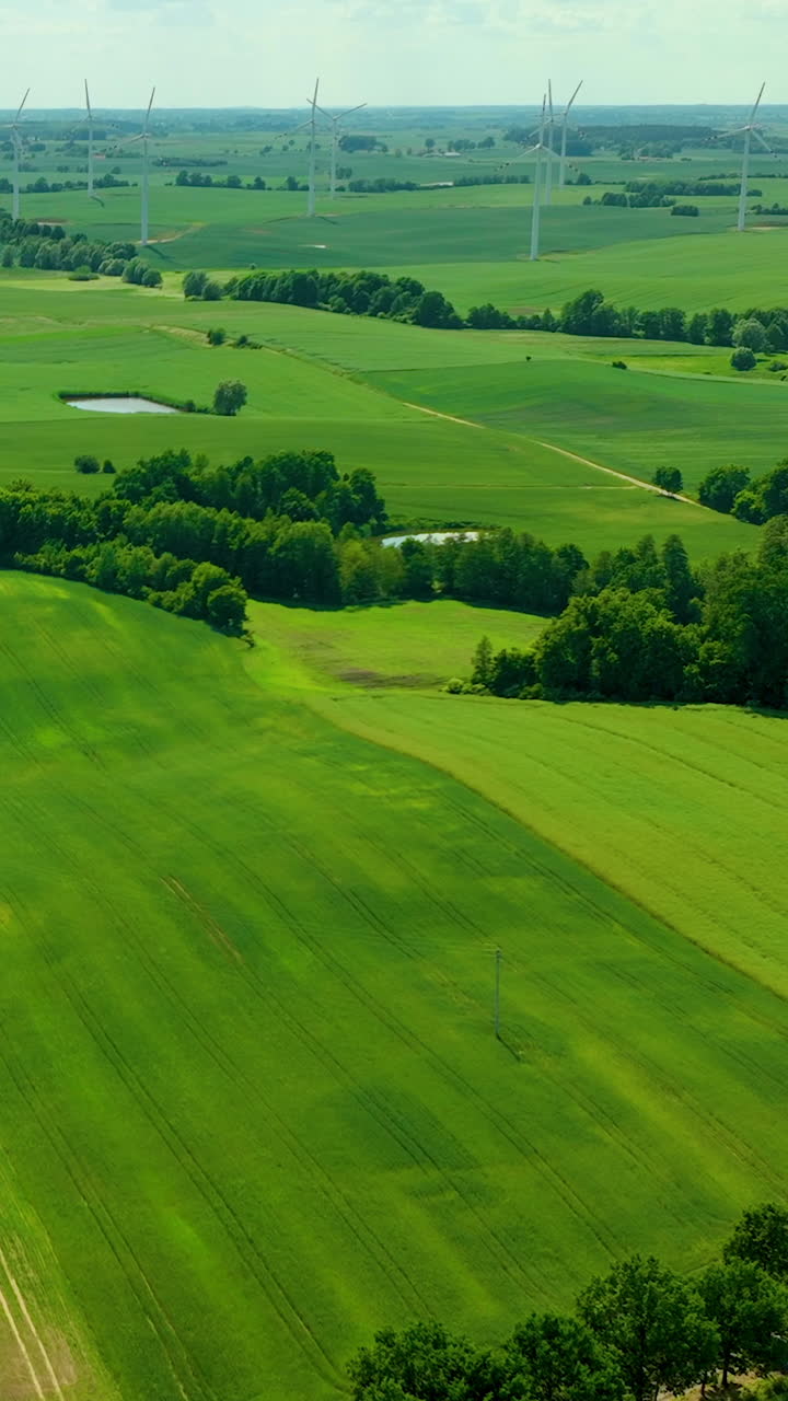Vertical aerial view of a wind farm integrated into a vibrant green agricultural landscape with rolling hills and trees. Ideal for sustainability and renewable energy social media content